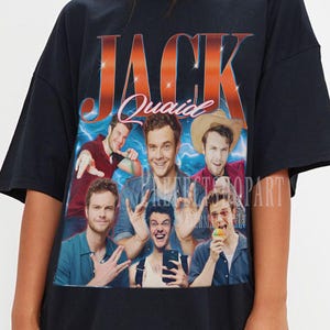 Op de afbeelding: Zwart T-shirt met een afbeelding van Jack Quaid, met de naam "JACK" in oranje en rode tekst. De afbeelding bevat meerdere afbeeldingen van Jack Quaid. Het T-shirt wordt door een persoon gedragen.