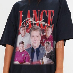 May include: Black oversized t-shirt with a graphic print of Lance Barber from the TV show "Superstore". The graphic features a collage of photos of Lance Barber in different scenes from the show. The text "LANCE Barber" is printed in red on the shirt.