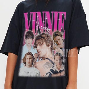May include: Black t-shirt featuring a graphic of Vinnie Hacker with the text "Vinnie Hacker" in pink. The shirt has a vintage, faded look, with multiple images of Vinnie Hacker. The shirt is a casual, oversized style.
