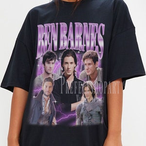 Op de afbeelding: Zwart oversized T-shirt met een paarse grafische print van Ben Barnes. De grafiek bevat meerdere afbeeldingen van Ben Barnes in verschillende rollen, met paarse bliksemschichten op de achtergrond. De tekst "Ben Barnes" is gedrukt in grote, vetgedrukte, paarse letters.