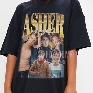 May include: Black oversized t-shirt with a graphic print of a group of young men. The graphic features the text "Asher Angel" in gold lettering.