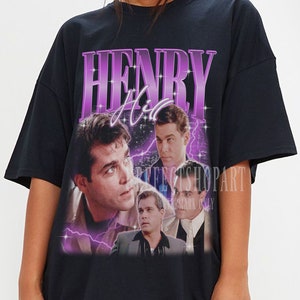 Puede incluir: Camiseta negra de gran tamaño con un estampado gráfico de Henry Hill de la película Goodfellas. El gráfico es en morado y rosa con un diseño de rayo. El texto "HENRY HILL" está impreso en letras moradas grandes.