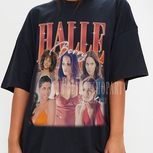 Peut inclure: T-shirt noire surdimensionnée avec un imprimé graphique de Halle Berry dans un collage d'images. Le texte "Halle Berry" est imprimé en rouge et orange.