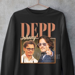 Könnte beinhalten: Schwarzer Pullover mit einem Vintage-Grafikdruck von Johnny Depp. Die Grafik zeigt ein Porträt von Depp mit dem Text "DEPP" und "Johnny" in brauner Schrift.