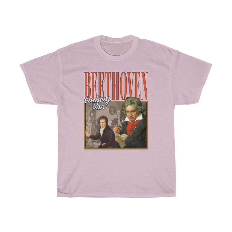 Pu&ograve; includere: Una t-shirt rosa chiaro con una grafica in stile vintage di Ludwig van Beethoven. La grafica presenta un ritratto di Beethoven e il testo "BEETHOVEN Ludwig Van" in rosso e bianco.