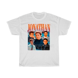 Peut inclure: T-shirt blanc avec un graphique de style vintage repr&eacute;sentant un groupe d'hommes avec le texte "Jonathan Bailey" dans une police r&eacute;tro color&eacute;e.