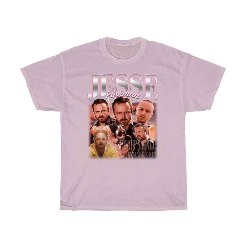 May include: Pink t-shirt with a graphic of Jesse Pinkman from the TV show Breaking Bad. The graphic features multiple images of Jesse in different poses, including one with a gun. The text "Jesse Pinkman" is written in pink and silver letters.