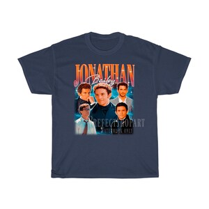 Peut inclure: Un t-shirt bleu marine avec un motif vintage repr&eacute;sentant un groupe d'hommes avec le texte "Jonathan Bailey" dans une police r&eacute;tro color&eacute;e.