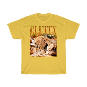 May include: Mustard yellow t-shirt displaying the word "GLUTEN" in gold, with an image of bread and wheat. The words "gluten free" are also visible. The shirt is made of a soft, comfortable material.