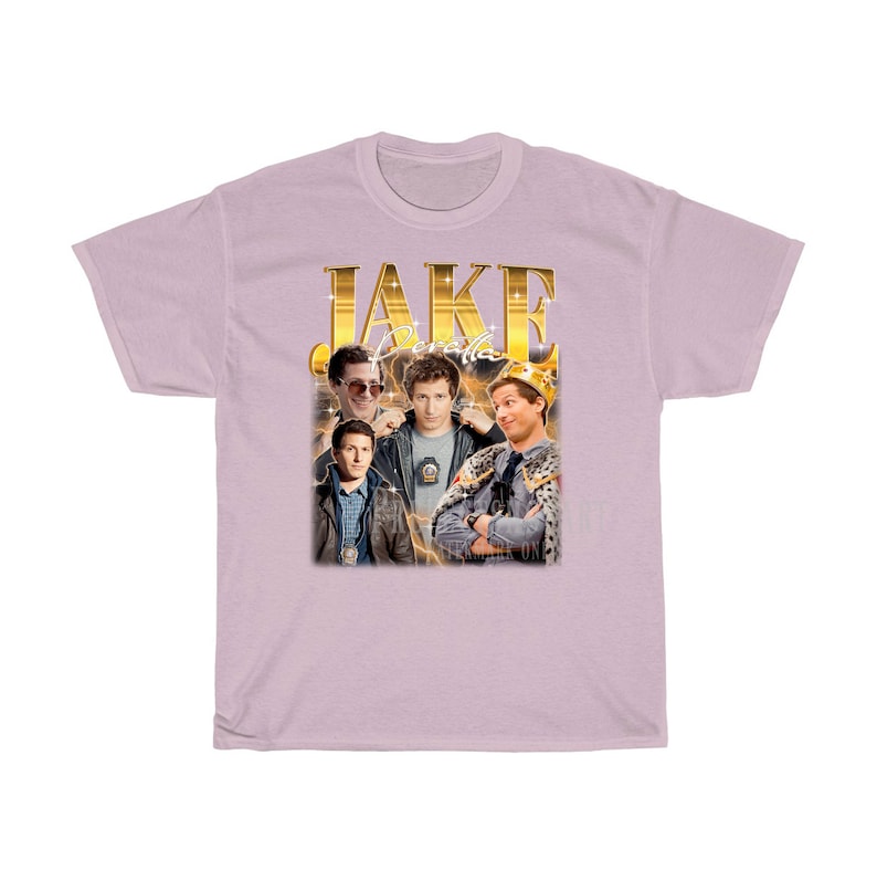 May include: A light pink t-shirt with a gold graphic of Jake Peralta from the TV show Brooklyn Nine-Nine. The graphic includes the text "JAKE PERALTA" and features multiple images of Jake Peralta in different poses.