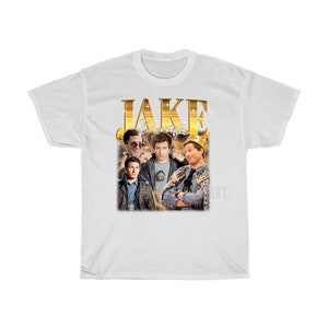 May include: White t-shirt with a gold graphic of Jake Peralta from the TV show Brooklyn Nine-Nine. The graphic includes the text "JAKE" and "Peralta" in gold letters.