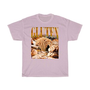May include: A lilac t-shirt with a gold-coloured "GLUTEN" graphic above an image of bread and wheat. The words "gluten free" are also visible. The design suggests a theme of gluten-free food.