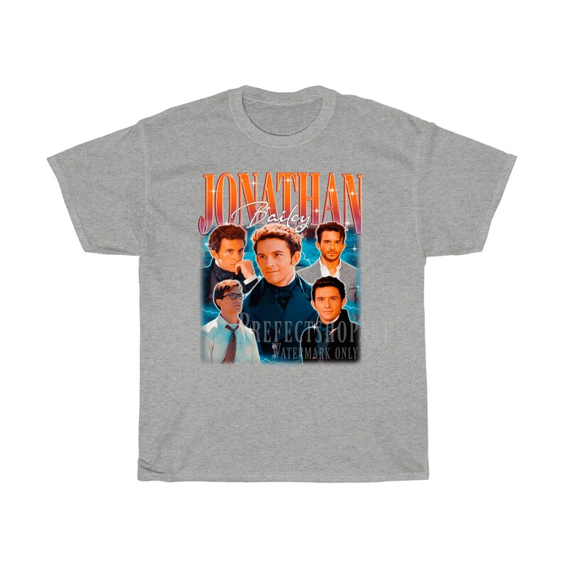 Peut inclure: T-shirt gris avec un graphique de style vintage repr&eacute;sentant un groupe d'hommes avec le texte "Jonathan Bailey" dans une police rouge et orange.