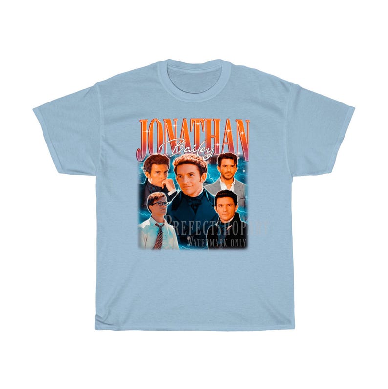 Peut inclure: T-shirt bleu clair avec un graphique de style vintage repr&eacute;sentant un groupe d'hommes avec le texte "Jonathan Bailey" dans une police rouge et orange.