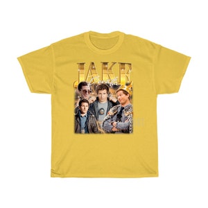 May include: Yellow t-shirt with a retro-style graphic of Jake Peralta from the TV show Brooklyn Nine-Nine. The graphic features Jake Peralta in different poses with the text "JAKE PERALTA" in gold letters.