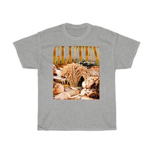 May include: A grey t-shirt with a graphic that reads "GLUTEN FREE" in gold. The graphic shows different types of bread and wheat, suitable for those with dietary restrictions.
