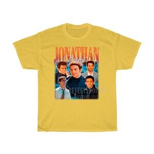 Peut inclure: T-shirt jaune avec un graphique de style vintage repr&eacute;sentant un groupe d'hommes avec le texte "Jonathan Bailey" en rouge et jaune.