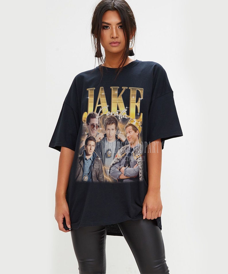 May include: Black oversized t-shirt with a graphic print of the characters from the TV show "Brooklyn Nine-Nine". The graphic features the characters Jake Peralta, Amy Santiago, Charles Boyle, Rosa Diaz, and Captain Raymond Holt. The text "JAKE PERALTA" is printed in gold letters on the shirt.