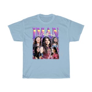 May include: Light blue t-shirt with a retro-style graphic featuring a group of four girls. The graphic includes the text "IMAN" in a purple and pink font.