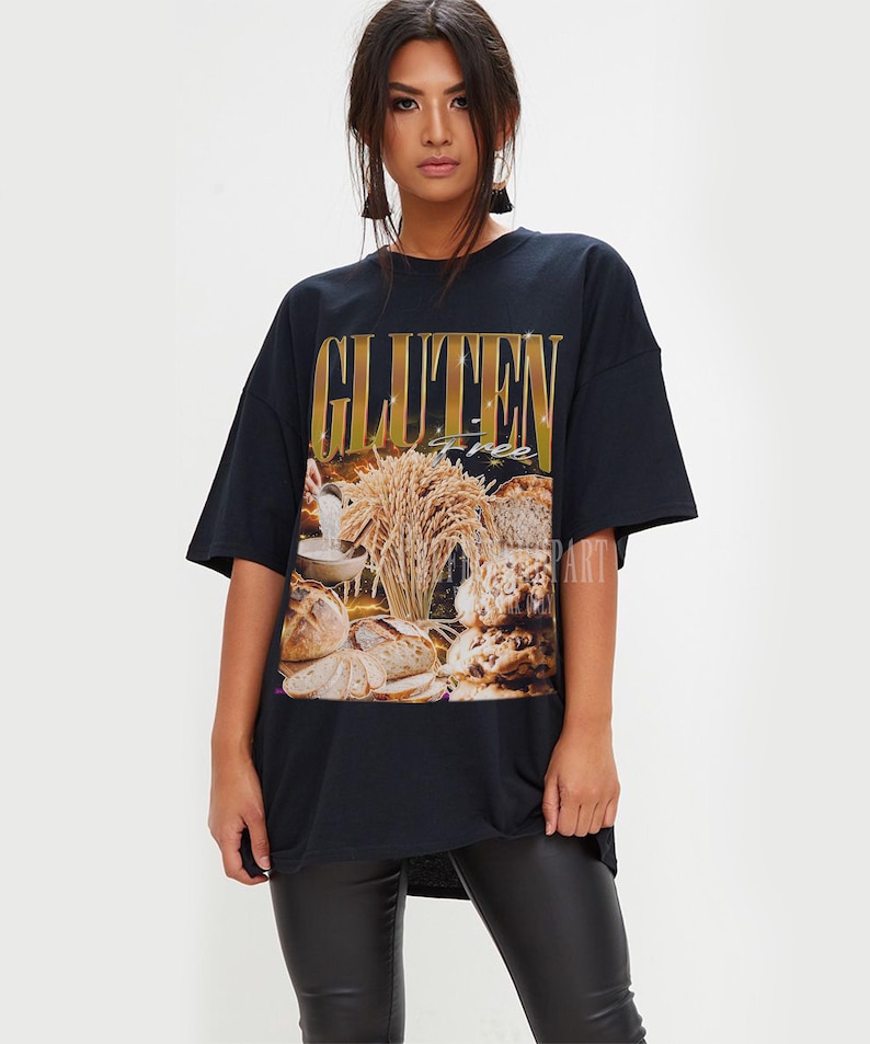 May include: Black t-shirt with a gold-coloured "GLUTEN" text and a graphic of bread and wheat. The shirt has a loose fit. The word "free" is also visible.
