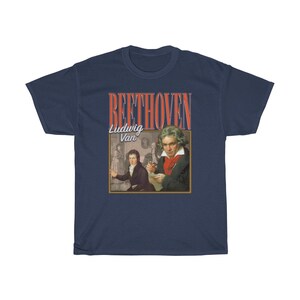 Pu&ograve; includere: Una t-shirt blu navy con una grafica in stile vintage di Ludwig van Beethoven. La grafica presenta un ritratto di Beethoven e il testo "BEETHOVEN" in rosso e bianco.