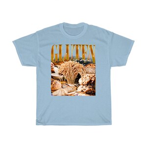 May include: Pale blue t-shirt featuring the words "GLUTEN FREE" in gold. The graphic shows different types of bread, wheat, and a bowl of flour. The shirt is made of a soft, comfortable material.