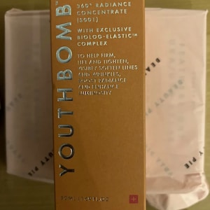 May include: A gold box with the text "Youth Bomb" in silver lettering. The box is labeled "360&deg; Radiance Concentrate (5001)" and "With Exclusive Biolog-Elastic Complex". The box also says "To help firm, lift and tighten, visibly soften lines and wrinkles, boost radiance and enhance luminosity". The box is 50 ml (1.69 fl oz) and has a small Swiss flag on the bottom right corner.