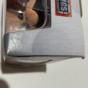 May include: A partially visible product package with the text "METALFIGS" in a rectangular frame. The package is silver with a clear plastic window. The product inside is partially visible.