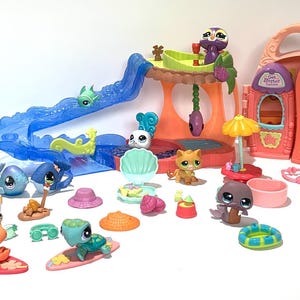 Peut inclure: Une collection de figurines d'animaux en plastique Littlest Pet Shop et d'ensembles de jeu, incluant une arche d'aquarium bleue, un toboggan bleu, une cabane dans les arbres et un bâtiment pêche. Divers petits accessoires comme des planches de surf sont inclus.