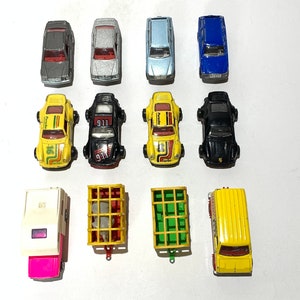Op de afbeelding: Een verzameling vintage speelgoedauto's en -trucks, waaronder een gele camper, een gele schoolbus, een zwart-gele sportwagen, een blauwe auto, een zilveren auto en een grijze auto.