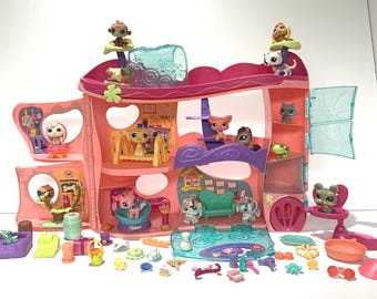 May include: A multi-level pink and orange plastic toy playset featuring various rooms, balconies, and a translucent blue roof section. The set includes numerous small animal figurines, miniature furniture pieces, and accessories scattered around the base.