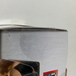 May include: A partially visible action figure in a clear plastic case. The figure has a black and tan color scheme. The packaging has a white background with the words "METALFIG" in a red and silver design.