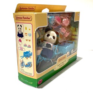 May include: A Sylvanian Families Cycle & Skate Set Panda Girl toy in a cardboard box. The set includes a flocked panda figure, a light blue bicycle with a front basket, a matching light blue trailer, pink roller skates, and various accessories.