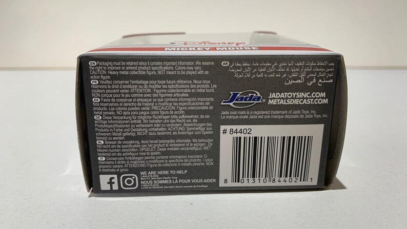 May include: A black and gray box with text including "MICKEY MOUSE" and "Jada Toys." The box has a barcode and the number 84402. The box contains a collectible figure.