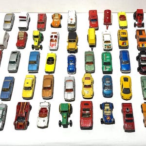 Può includere: Una collezione di macchinine giocattolo in vari colori, tra cui rosso, giallo, blu e verde. I veicoli in miniatura sono disposti su una superficie bianca, mostrando una varietà di modelli e stili di auto. Alcune auto hanno dettagli visibili.