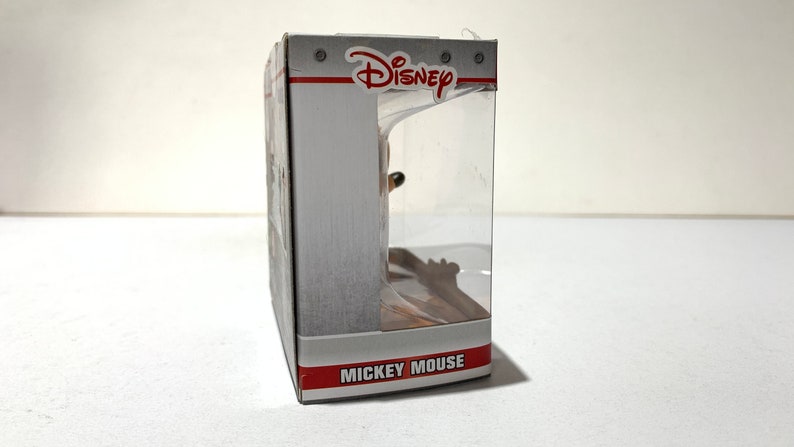 May include: A Disney-branded product box with a clear plastic window. The box is primarily white with red and gray accents. The Disney logo is visible at the top, and the words "Mickey Mouse" are printed on the bottom.