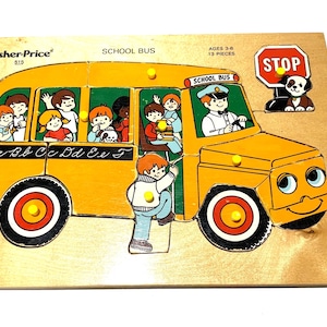 Op de afbeelding: Een houten Fisher-Price puzzel met knoppen, voorzien van een gele schoolbus met een chauffeur, passagiers en een stopbord. De bus heeft een lachend gezicht aan de voorzijde, zwarte wielen met rode en gele centra en de letters Aa tot Ff gedrukt.