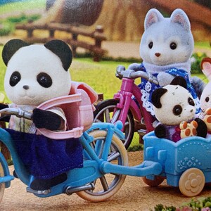 May include: A panda figure with a pink backpack rides a blue bicycle with a front basket containing a yellow bottle and a blue bear-shaped item. A blue trailer attached to the bike carries a small panda figure and a white rabbit figure.