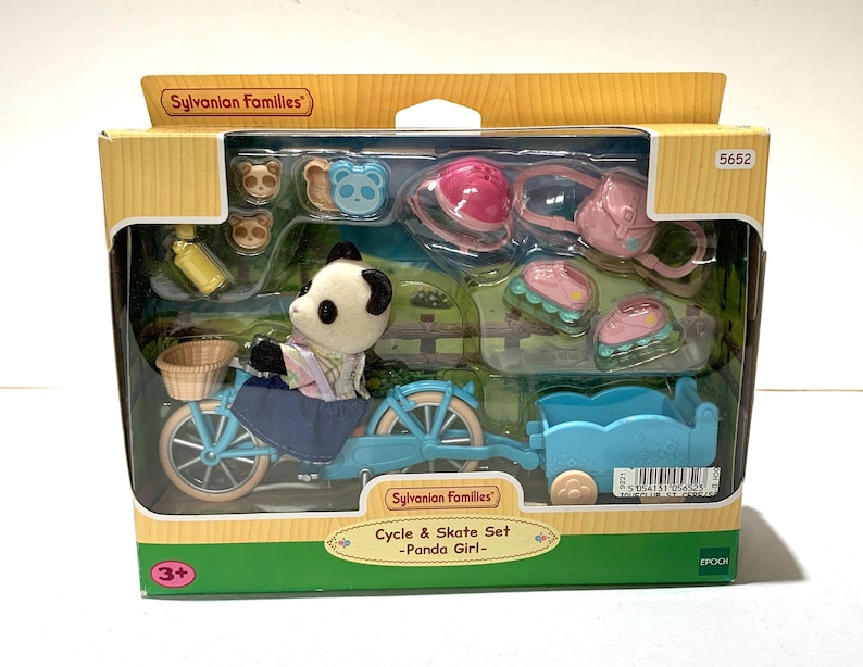 May include: A Sylvanian Families Cycle & Skate Set featuring a panda figure on a light blue bicycle with a matching trailer. The set includes a pink helmet, a pink backpack, two pairs of roller skates, a yellow water bottle, and small accessories.