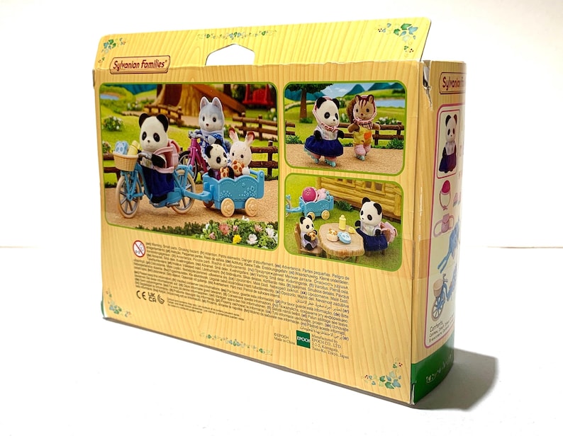 May include: A Sylvanian Families toy box featuring illustrations of panda and rabbit figures with a blue bicycle and trailer. The packaging displays various scenes of the animal characters in a miniature outdoor setting with printed text.