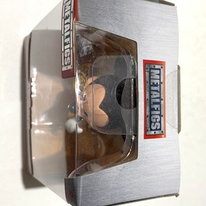 May include: A boxed collectible figure of a cartoon character. The figure is visible through a clear plastic window. The box is silver with red and white text that reads "METALFIGS". The figure is black, tan, and white.