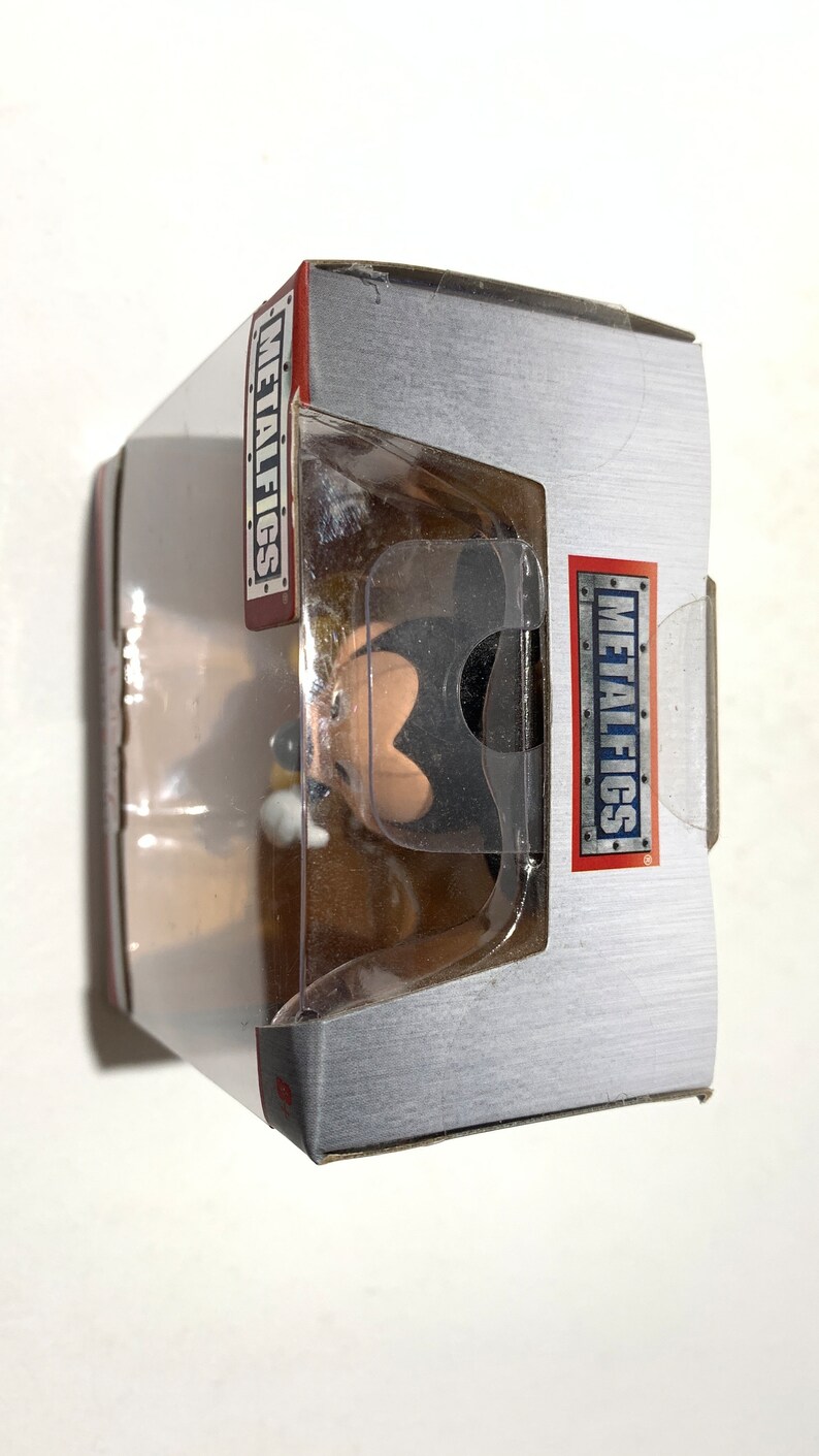 May include: A boxed collectible figure of a cartoon character. The figure is visible through a clear plastic window. The box is silver with red and white text that reads "METALFIGS". The figure is black, tan, and white.