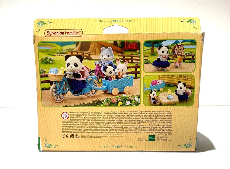 May include: A Sylvanian Families toy set box featuring a panda figure on a light blue bicycle with a matching trailer. The box displays various scenes of animal figures, including a panda, a wolf, and a rabbit, engaged in outdoor activities.
