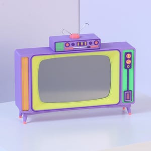 May include: A purple television set with a lime green screen frame, an orange side panel, and a small rectangular top unit featuring a pink circular knob and two thin metal antennas. The device stands on four small legs and has orange control dials.