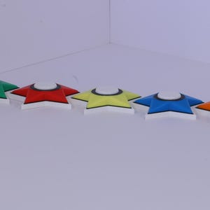 May include: Five star-shaped objects in a row, each with a white base and a colored top. The colors are green, red, yellow, blue, and orange. Each has a white circle in the center.
