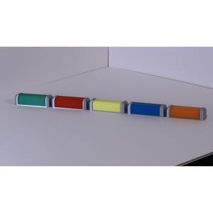 May include: Five brightly coloured rectangular objects with silver rounded ends. The objects are green, red, yellow, blue, and orange. They are arranged in a row on a white surface.