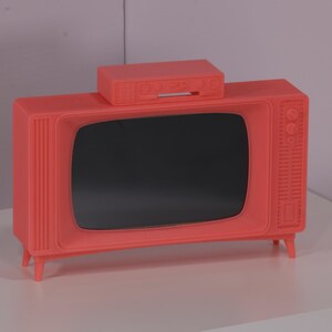 May include: A vintage-style, bright pink television set with a matching pink top. The television has a black screen and is sitting on a white surface.