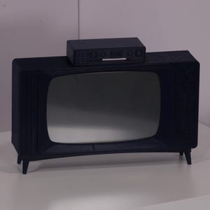Peut inclure: Un téléviseur vintage noir avec un petit boîtier noir sur le dessus. Le téléviseur est posé sur une surface blanche.