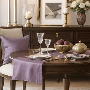 May include: A dining table set for a meal. The round, dark wood table is set with plates, silverware, and a purple runner. A chair with a purple pillow sits nearby. A decorative bowl of fruit and a gold-colored sugar bowl are on the table.