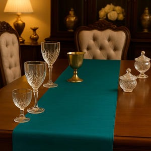 May include: A formal dining table setting with a teal runner, crystal glassware, a gold goblet, and two small glass jars with lids. The scene is illuminated by a warm lamp and set against a dark wood background.